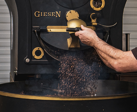 Foto von offener Klappe des Giesen Kafferösters, aus der geröstete Kaffeebohnen fallen.